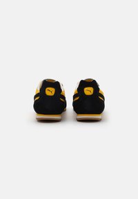 Crne i žute suede tenisice imaju niski profil, kontrastne pruge i gumu potplate s Puma logotipom na peti.