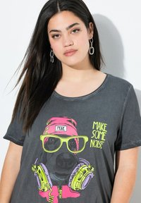 T-shirt gris à manches courtes avec un graphique d'un chien portant des lunettes de soleil et des écouteurs. Le texte indique "FAITES DU BRUIT" dans des couleurs néon.