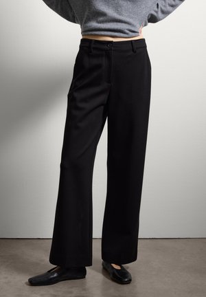 Zwarte wijde broek van soepel materiaal, met een knoopsluiting, zijzakken en een getailleerd ontwerp. Draag hem met platte zwarte schoenen.