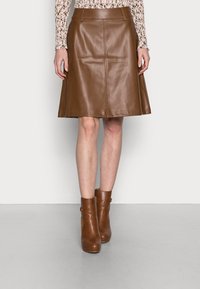 Bruine leren flared rok met een gladde textuur, tailleband en naaddetails, gecombineerd met bruin leren enkellaarsjes van glanzend leer.