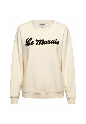 Crèmekleurige crewneck-trui met lange mouwen en zwarte cursieve tekst "Le Marais" op de borst.