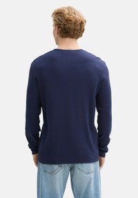 Navyblauw long sleeve top met een gestructureerde stof, ronde hals en een iets getailleerde pasvorm, gecombineerd met lichtgekleurde jeans.