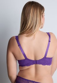 Soutien-gorge en dentelle violette avec des bretelles satinées ajustables et un bord en dentelle festonné. Fermeture au dos avec un crochet et un œil.