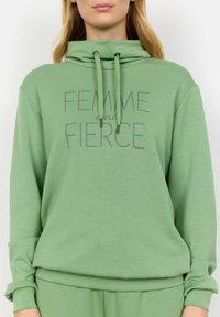 Grön sweatshirt med funnel neck, med tryckt text "FEMME and FIERCE" i grått. Tillverkad av mjukt tyg med en avslappnad passform.