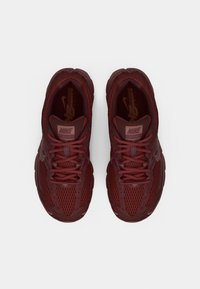 Nike tenisky v burgundskej farbe s hornou časťou z mäkkej sieťoviny, okrúhlou špičkou, plochými šnúrkami a logom na jazyku. Obsahujú textúrované panely a gumovú podrážku.
