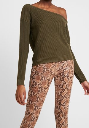 Olivgrüner, gerippter Strickpullover mit einem schulterfreien Design, kombiniert mit eng sitzenden Schlangenlederhosen in Braun- und Beigetönen.