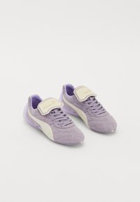 Purple suede sneakers with a white side stripe, adjustable velcro strap, and textured rubber sole. Gold lettering on strap.