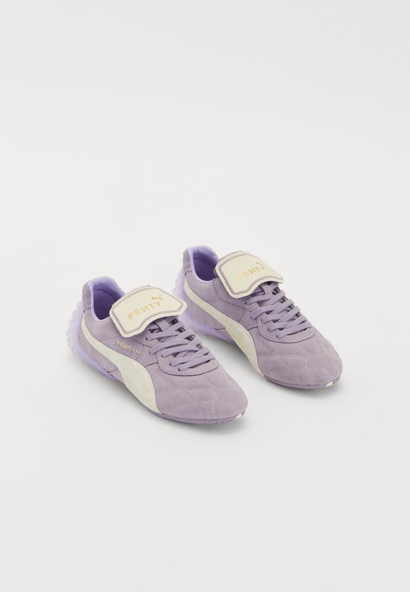 Purple suede sneakers with a white side stripe, adjustable velcro strap, and textured rubber sole. Gold lettering on strap.