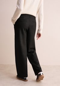 Zwarte, wijde broek van een gestructureerd, sprankelend materiaal met een vlakke tailleband, gecombineerd met zwarte schoenen met witte accenten.
