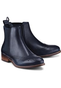 Námořnické kožené kotníkové boty s brogue detaily, elastickými postranními panely a poutkem na patě. Hnědý vysoký podpatek a kontrastní bílé švy.