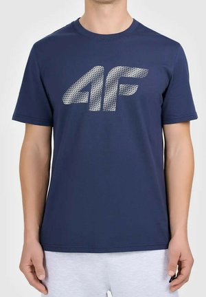 Man draagt een donkerblauw T-shirt met een getextureerd wit "4F"-logo op de borst en lichtgrijze korte broek tegen een effen achtergrond.