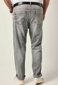 Jeans in denim grigio con una vestibilità ampia, dotati di tasche posteriori e risvolto. Accompagnati da una cintura nera e sneakers bianche.