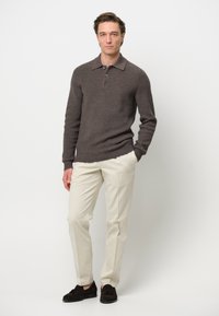 Suéter de polo de punto acanalado marrón oscuro, pantalones crema y mocasines de ante oscuros. El suéter cuenta con un cuello y tres botones. Fondo liso.