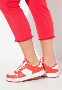 Röda och vita sneakers har en slät läderdesign, rundad form, platt sula och kontrasterande detaljer på sidan och hälen.