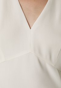 Gros plan d'une personne portant un vêtement blanc à col en V avec des détails de couture visibles et une texture de tissu lisse.