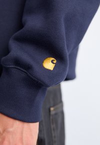Marineblauwe sweatshirt met een geribbelde manchette en een gouden geborduurd logo op de mouw. Gemaakt van gestructureerde stof voor warmte.