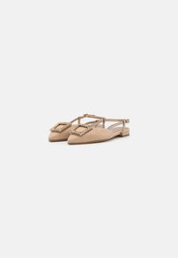 Beige slingback flats with a pointed toe, textured fabric, and a decorative beige and gold buckle on the upper. Flat wooden sole.
