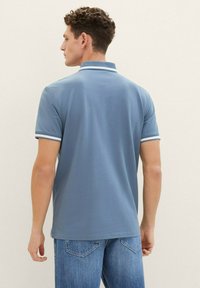 Ljusblå polo t-shirt med kort ärm, vita detaljer vid kragen och ärmsluten, samt en texturerad tyg. Bärs med blå denimjeans.