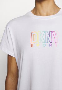 White cotton t-shirt with short sleeves, featuring a multi-colored "DKNY SPORT" logo in gradient text across the chest.