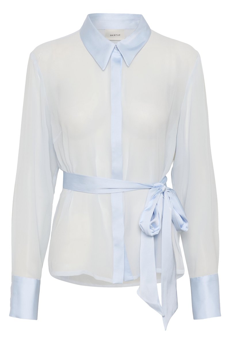 Lichtblauwe blouse met lange mouwen, puntige kraag, knoopsluiting, brede manchetten en een gebonden satijnen tailleceintuur aan de rechterkant.