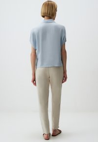 Lichtblauwe blouse met korte mouwen en een kraag, gecombineerd met crème-kleurige, losse broek en sandalen, gezien vanuit de achterkant.