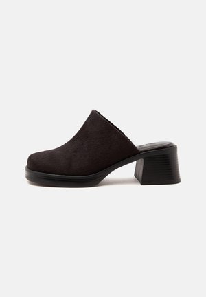 Mule noire à talon avec un bout fermé arrondi et un talon bloc épais sur fond blanc uni.