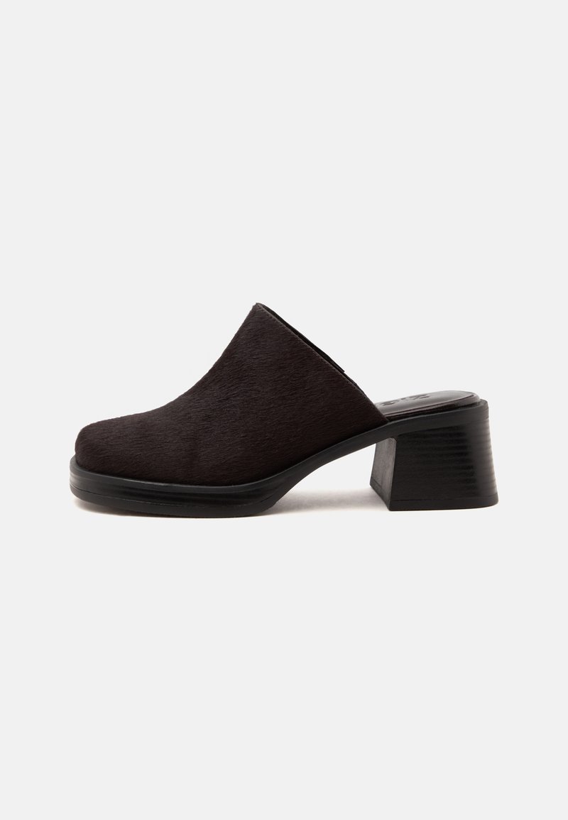Mule noire à talon avec un bout fermé arrondi et un talon bloc épais sur fond blanc uni.
