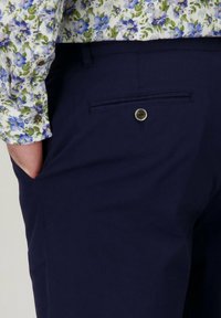 Marineblauwe broek met een rechte voorkant, zijzakken en een achterzak met een knoop. De stof is soepel en heeft een slim fit.