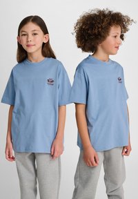 Jasnoniebieskie bawełniane koszulki z krótkimi rękawami i okrągłym dekoltem, z małym czerwonym logo na klatce piersiowej. W zestawie z szarymi dresami.