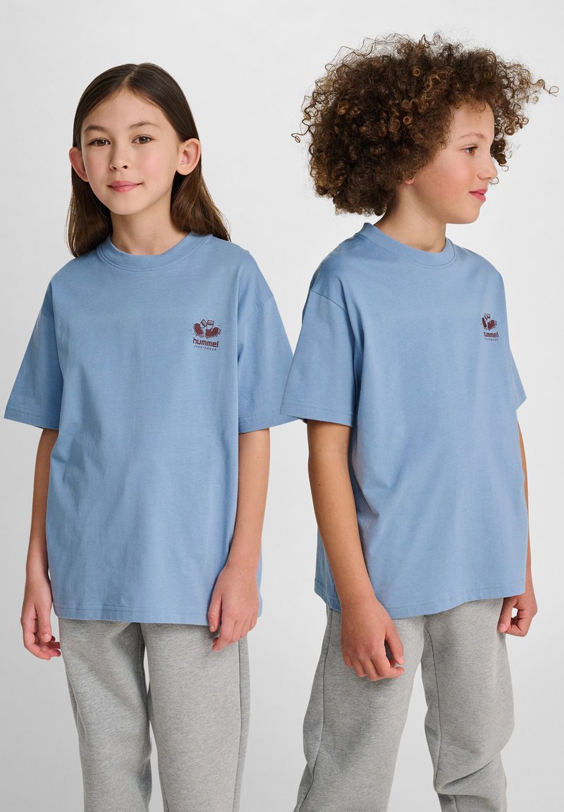 Jasnoniebieskie bawełniane koszulki z krótkimi rękawami i okrągłym dekoltem, z małym czerwonym logo na klatce piersiowej. W zestawie z szarymi dresami.