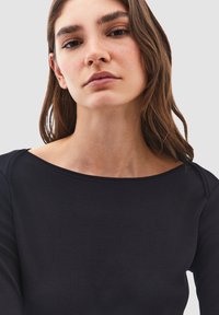 Maglietta nera a maniche lunghe con scollatura ampia. Tessuto morbido con una texture liscia, design aderente che enfatizza le spalle. Stile minimalista.