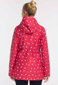 Červená dešťová bunda s bílými puntíky, s kapucí, dlouhými rukávy a volným střihem. Hladká, lesklá textura, vhodná do vlhkého počasí.