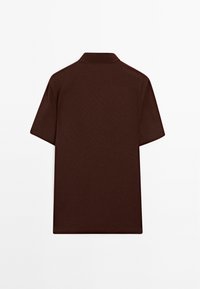 Brun kortärmad polotröja med klassisk krage och en mjuk, texturerad tyg. Baksidan är enkel utan mönster eller accent.