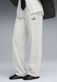 Grå sweatpants i en bomullsblandning med avslappnad passform, med sidfickor och en liten svart Puma-logotyp på låret. Svarta skor nedanför.