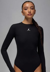 Bodysuit noir à manches longues en matériau lisse, présentant un logo Jordan blanc sur la poitrine et un design de jambe haute.