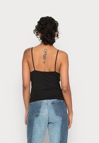 Camisola preta ajustada com alças finas, emparelhada com jeans de ganga azuis com detalhes de painel em contraste e detalhes de bolso, vista a partir das costas.