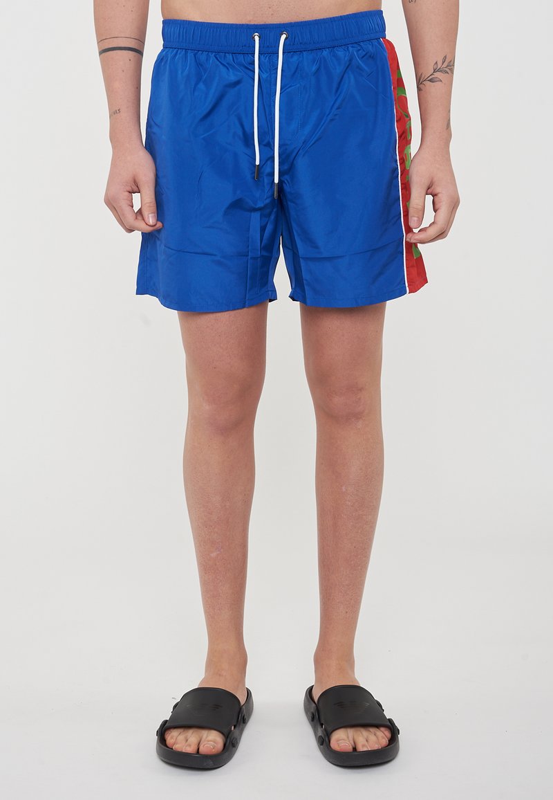 Shorts de bain bleus avec une taille élastique et un cordon de serrage blanc. Les accents latéraux présentent des motifs rouges et verts. Le matériau semble léger et lisse.