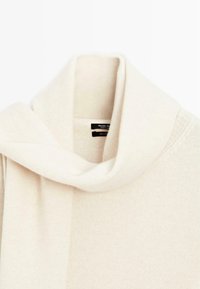 Cream-colored cashmere scarf with a loose, wide loop and a visible black clothing label inside the fold.