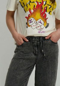 T-shirt graphique crème avec un texte jaune audacieux et un design de dés colorés. Associé à un pantalon à cordon de serrage noir avec un tissu texturé.