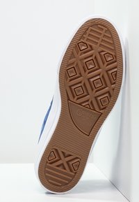 Brown rubber sole with diamond pattern, white sidewalls, and blue textured fabric upper. "Converse All Star" branding is visible on the sole.