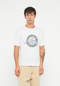 Hvit bomulls t-skjorte med rund hals og korte ermer, prydet med en grønn grafisk logo i sirkulært design på forsiden.
