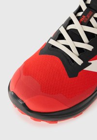 Chaussure de course rouge avec une tige en maille, des accents noirs et des lacets blancs. Présente une finition texturée et une semelle extérieure noire durable.
