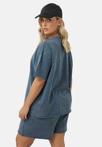 Niebieski dżinsowy t-shirt w oversize'owym kroju, z krótkimi rękawami i pasującymi szortami. Zawiera czapkę w kolorze czarnym, o gładkiej fakturze i luźnym kroju.