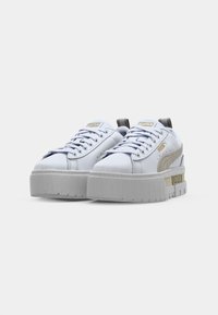 Sneaker Puma bianche con accenti a strisce beige e suole spesse e massicce, rivolte frontalmente su uno sfondo bianco semplice.