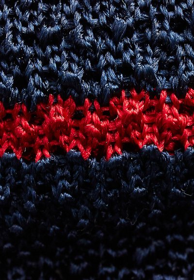 Marineblauer Strickstoff mit einem ausgeprägten roten Zickzack-Muster in der Mitte, das eine strukturierte, erhabene Oberfläche mit klaren Stichen zeigt.