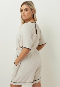 Beige linnéklänning med svarta pom-pom-detaljer, korta ärmar, elastisk midja, fickor och nyckelhål bak.