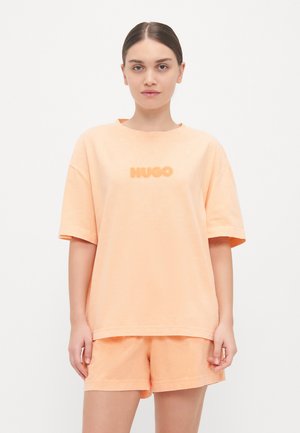 Krátký rukáv, oversized meruňkový tričko s tónovým logem "HUGO". Nosit s odpovídajícími meruňkovými šortkami vyrobenými z měkké bavlněné tkaniny.