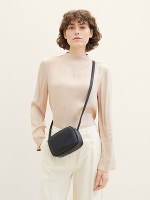 Borsa a spalla nera in pelle con finitura texture, forma rettangolare, manico corto e dettagli cuciti; indossata sopra una blusa di seta chiara.