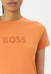 Orange cotton T-shirt with round neckline, short sleeves, featuring the word "BOSS" printed in a darker shade on the front.