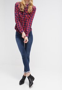 Röd och marinblå rutig skjorta med två bröstfickor, ihop med mörkblå skinnyjeans och svarta anklarstövlar. Släta tygstrukturer.